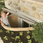 a young girl lifts an egress window well cover to safely escape basement