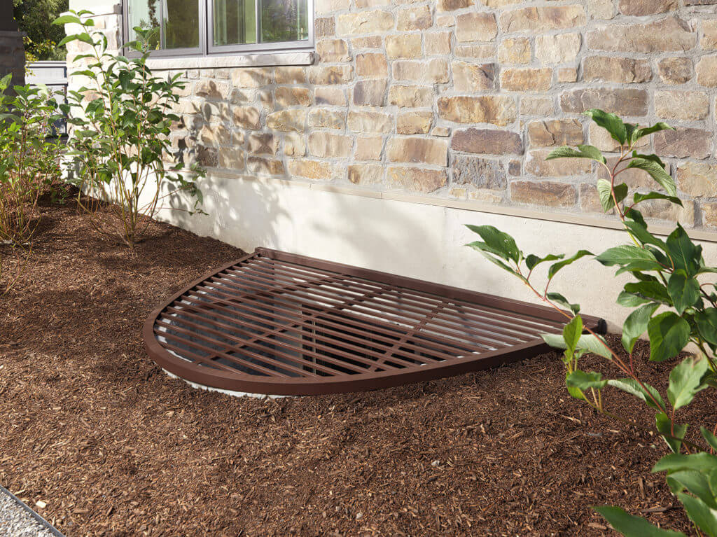 Rockwell egress window well with grate surrounded by landscaping egress solutions